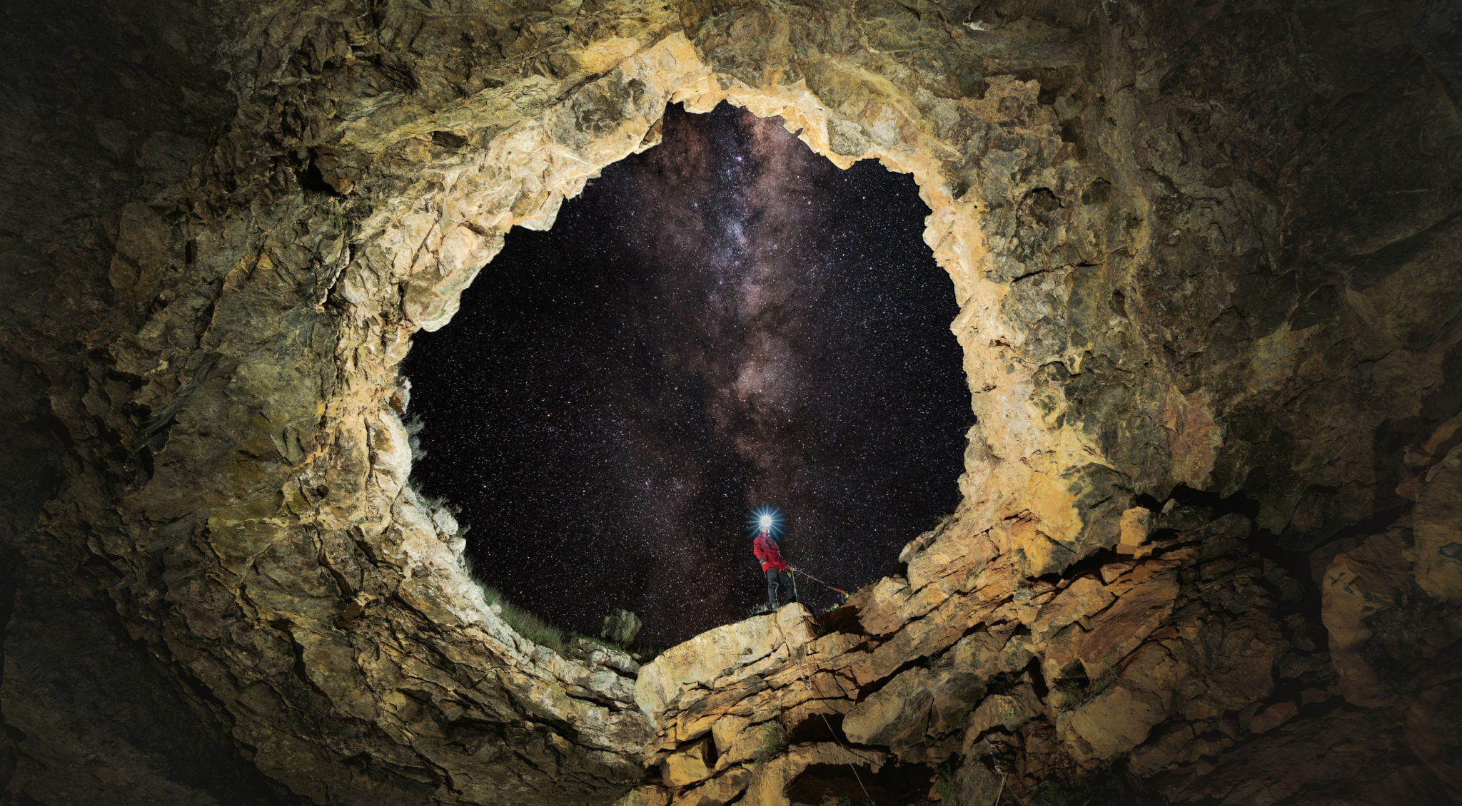 Caver standing at the entrance of a Nullarbor cave beneath the Milky Way, photographed from inside the cave.